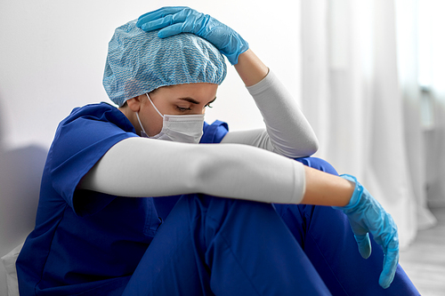 medicine, healthcare and pandemic concept - sad young female doctor or nurse wearing face protective mask for protection from virus disease holding to head