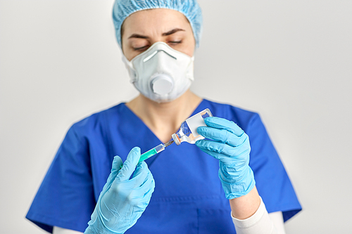 health, medicine and pandemic concept - female doctor or nurse wearing protective mask or respirator with syringe and drug in glass jar