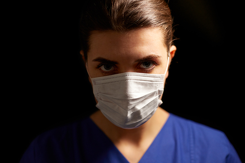 health, medicine and pandemic concept - young female doctor or nurse wearing face protective mask for protection from virus disease over black background