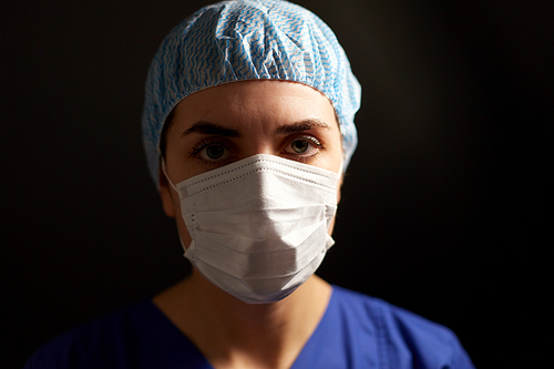 health, medicine and pandemic concept - young female doctor or nurse wearing face protective mask for protection from virus disease and hat over black background