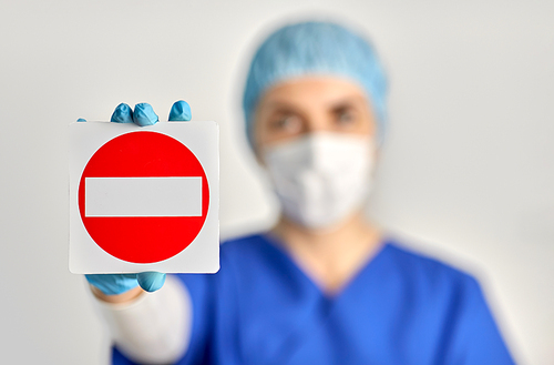 health, medicine and pandemic concept - young female doctor or nurse wearing face protective mask for protection from virus disease and hat showing stop sign over grey background