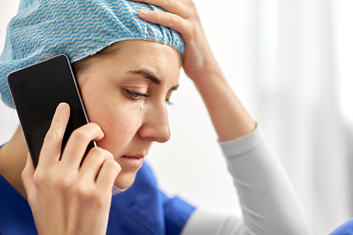 medicine, healthcare and pandemic concept - close up of sad young female doctor or nurse sitting on floor and calling on smartphone