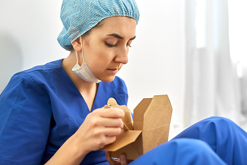 medicine, healthcare and pandemic concept - close up of sad and tired young female doctor or nurse eating takeaway food from disposable box sitting on floor at hospital