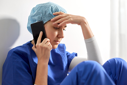 medicine, healthcare and pandemic concept - sad and tired young female doctor or nurse sitting on floor and calling on smartphone