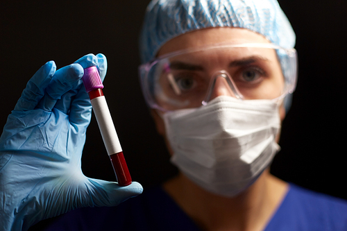 medicine, health and pandemic concept - close up of young female doctor or nurse wearing goggles, glove and face protective mask holding beaker with blood test over black background