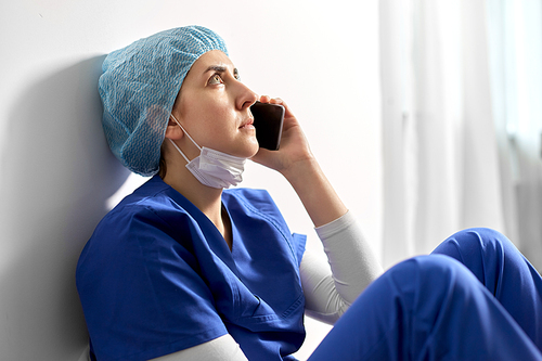 medicine, healthcare and pandemic concept - sad and tired young female doctor or nurse sitting on floor and calling on smartphone