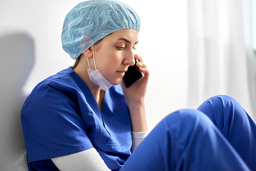 medicine, healthcare and pandemic concept - sad young female doctor or nurse sitting on floor and calling on smartphone