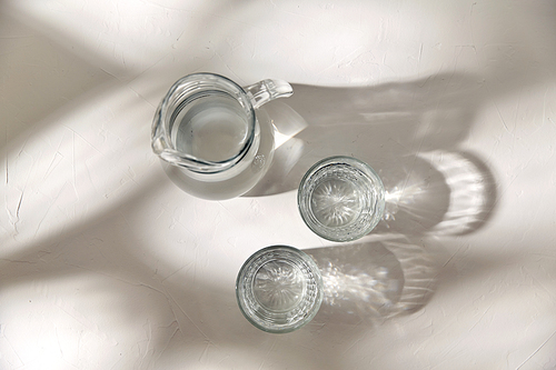 drink and glassware concept - two glasses and jug with water on white background with shadows
