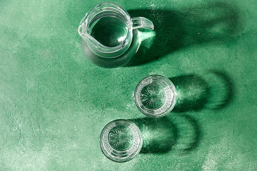 drink and glassware concept - two glasses and jug with water on emerald green background with shadows