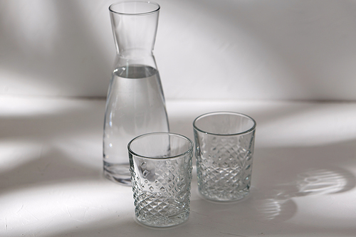 drink and glassware concept - two glasses and jug with water on white background with shadows