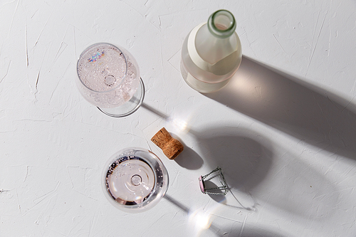 drink, alcohol and glassware concept - wine glasses and open champagne bottle dropping shadows on white surface