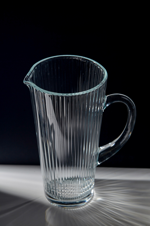 drink and glassware concept - empty faceted glass jug on table over black background