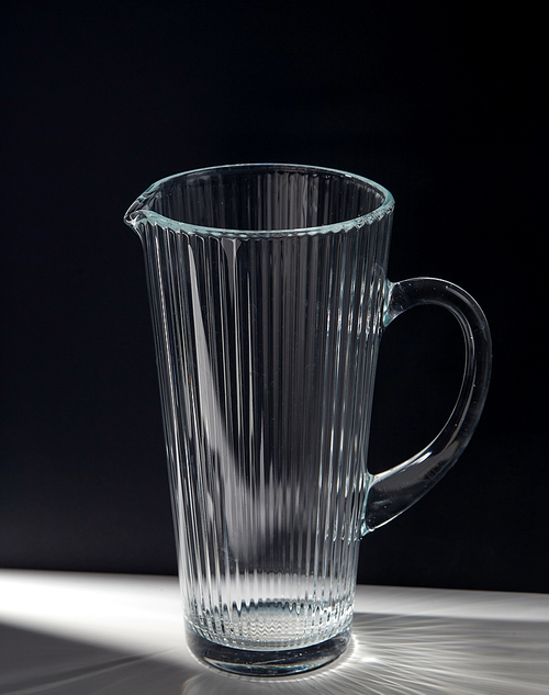 drink and glassware concept - empty faceted glass jug on table over black background