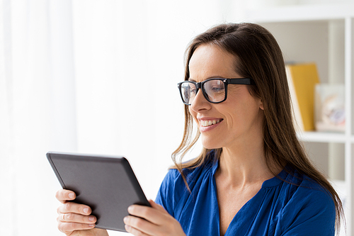 business, people and technology concept - happy smiling woman in glasses with tablet pc computer working at home or office
