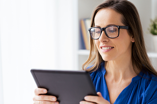 business, people and technology concept - happy smiling businesswoman in glasses with tablet pc computer working at home or office