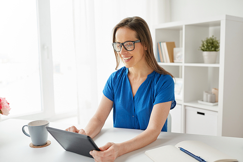 business, people and technology concept - happy smiling middle-aged woman in glasses with tablet pc computer working at home or office