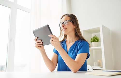 business, people and technology concept - happy smiling middle-aged woman in glasses with tablet pc computer working at home or office