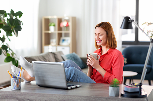 remote job, technology and people concept - happy smiling young woman with laptop computer and coffee having video call at home office with feet on table