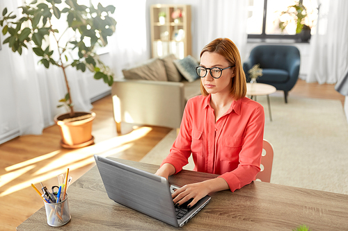 remote job, technology and people concept - young woman in glasses with laptop computer working at home office
