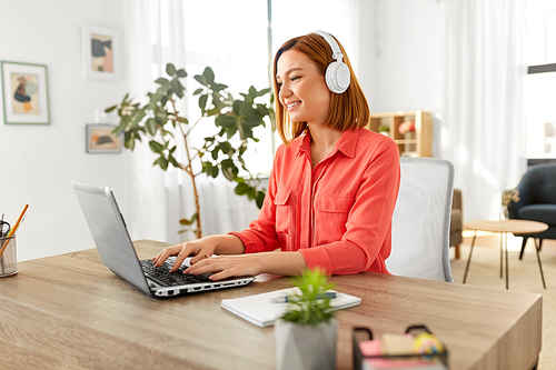 remote job, technology and people concept - happy smiling young woman in headphones with laptop computer working at home office