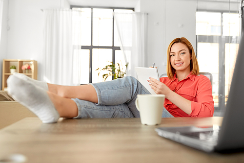remote job, technology and people concept - happy smiling young woman with notebook and laptop computer at home office resting feet on table