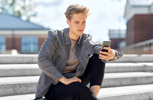 technology, communication and lifestyle concept - young man or teenage boy using smartphone in city