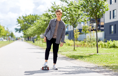 people and leisure concept - young man or teenage boy riding skateboard on city street