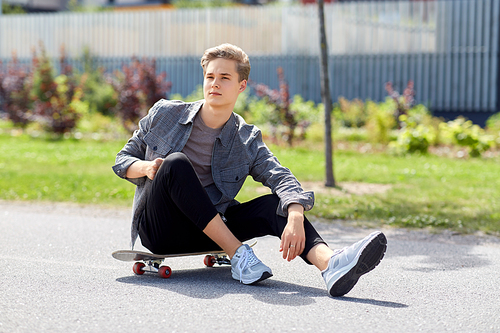 people and leisure concept - young man or teenage boy sitting on skateboard on city street