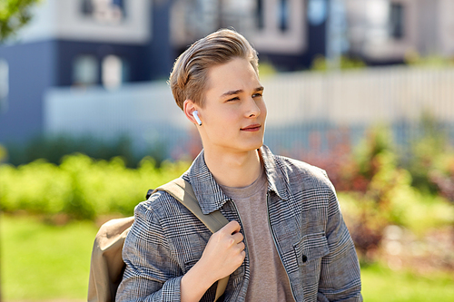 technology, leisure and people concept - young man or teenage boy with earphones and backpack walking in city