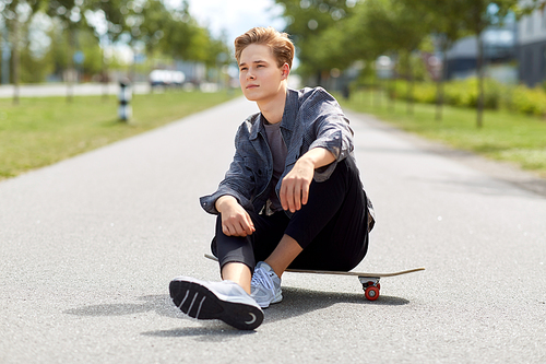people and leisure concept - young man or teenage boy sitting on skateboard on city street