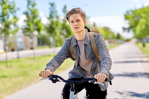 lifestyle, transport and people concept - young man or teenage boy with backpack riding bicycle on city street