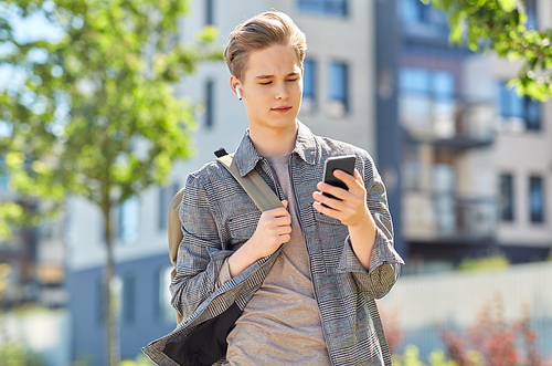 technology, leisure and people concept - young man or teenage student boy with smartphone, earphones and backpack in city