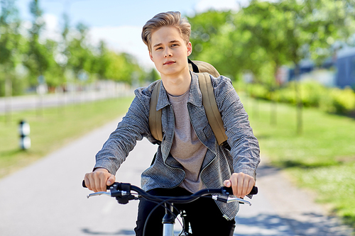 lifestyle, transport and people concept - young man or teenage boy with backpack riding bicycle on city street