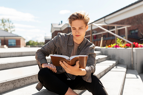 leisure, literature and people concept - young man or teenage boy reading book or diary in city