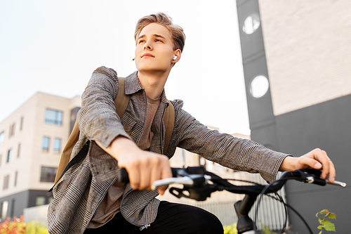 lifestyle, transport and people concept - young man or teenage student boy with earphones and backpack riding bicycle in city