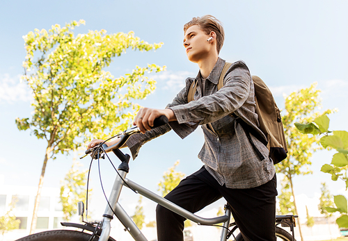 lifestyle, transport and people concept - young man or teenage student boy with earphones and backpack riding bicycle in city