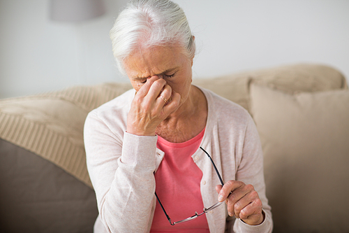 old age, health problem, vision and people concept - close up of senior woman with glasses sitting on sofa and having headache at home