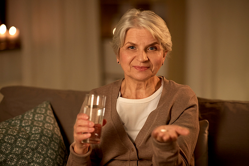 medicine, healthcare and old age concept - senior woman with pills and glass of water at home at night