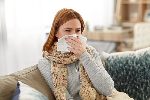 healthcare, cold, allergy and people concept - sick woman blowing her runny nose in paper tissue at home