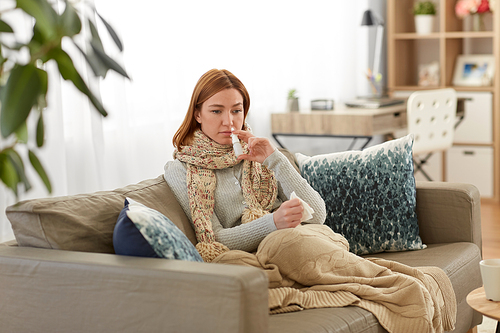 healthcare, cold and people concept - sick woman using nasal spray at home