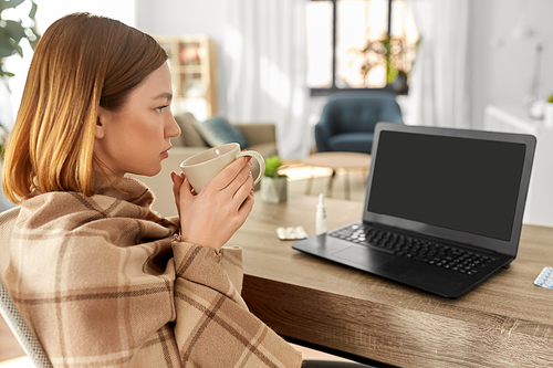 healthcare, technology and people concept - sick young woman in blanket drinking tea and having video call on laptop computer at home