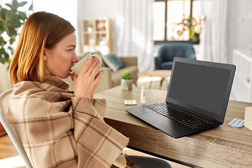 healthcare, technology and people concept - sick young woman in blanket drinking tea and having video call on laptop computer at home
