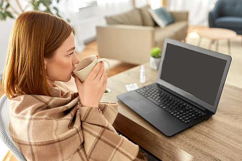 healthcare, technology and people concept - sick young woman in blanket drinking tea and having video call on laptop computer at home