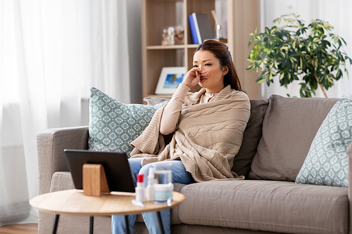 cold and health problem concept - sick asian woman with runny nose in blanket at home