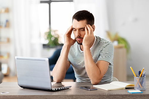 remote job, technology and people concept - stressed young man with laptop computer having headache at home office