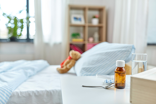 healthcare concept - medicine on table and teddy bear toy in bed at home