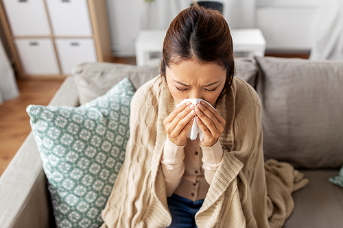 healthcare, cold and people concept - sick asian woman in blanket taking paper tissue from box and blowing her nose at home