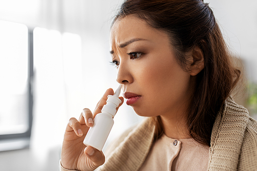 health, cold and people concept - sad sick young asian woman in blanket using nasal spray at home