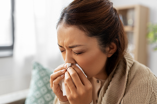 healthcare, cold and people concept - sick asian woman in blanket taking paper tissue from box and blowing her nose at home