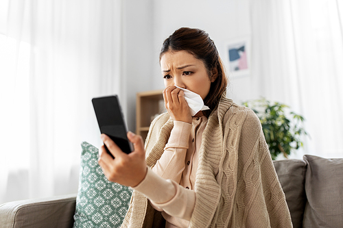 medicine, healthcare and technology concept - sick young asian woman having video call or online consultation on smartphone at home